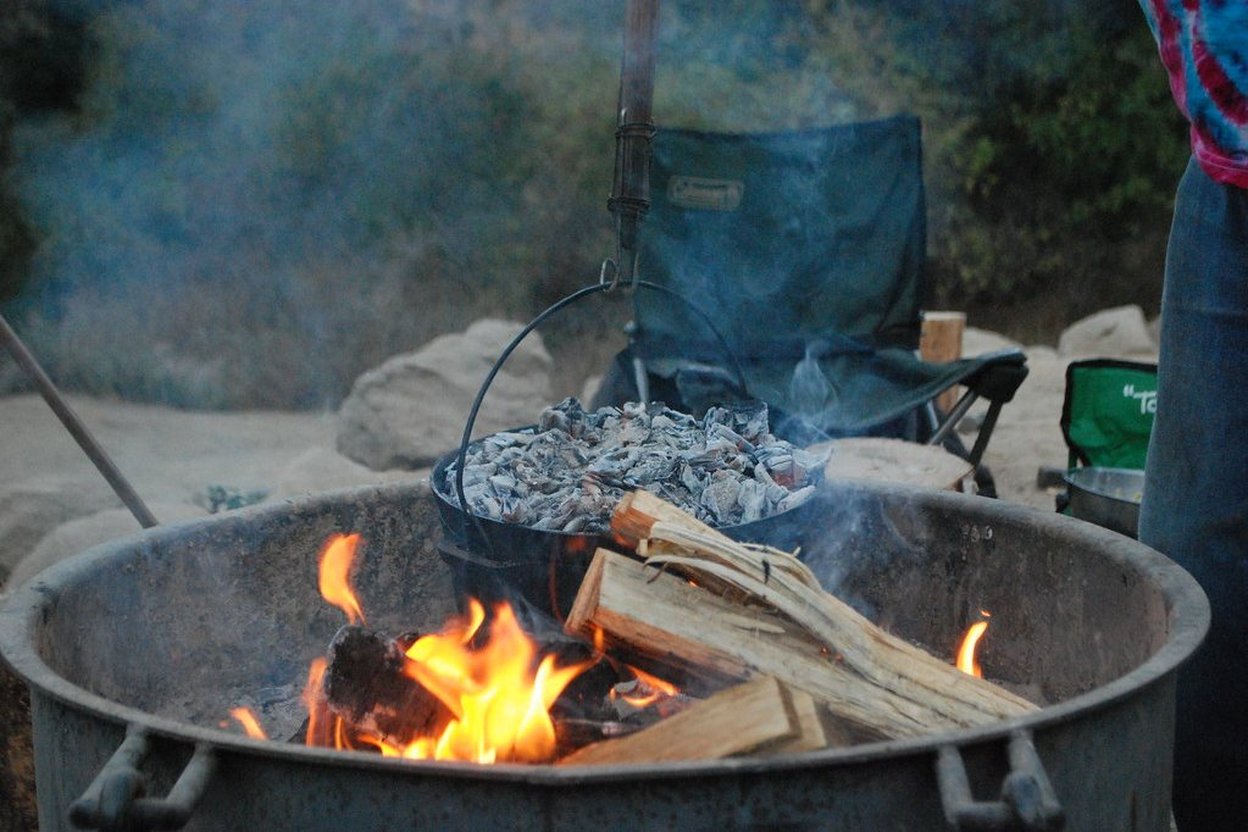 Campfire cooking with a Dutch oven over hot coals.