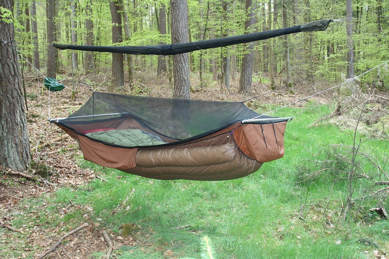 A camping hammock with a bug net and underquilt hung between trees