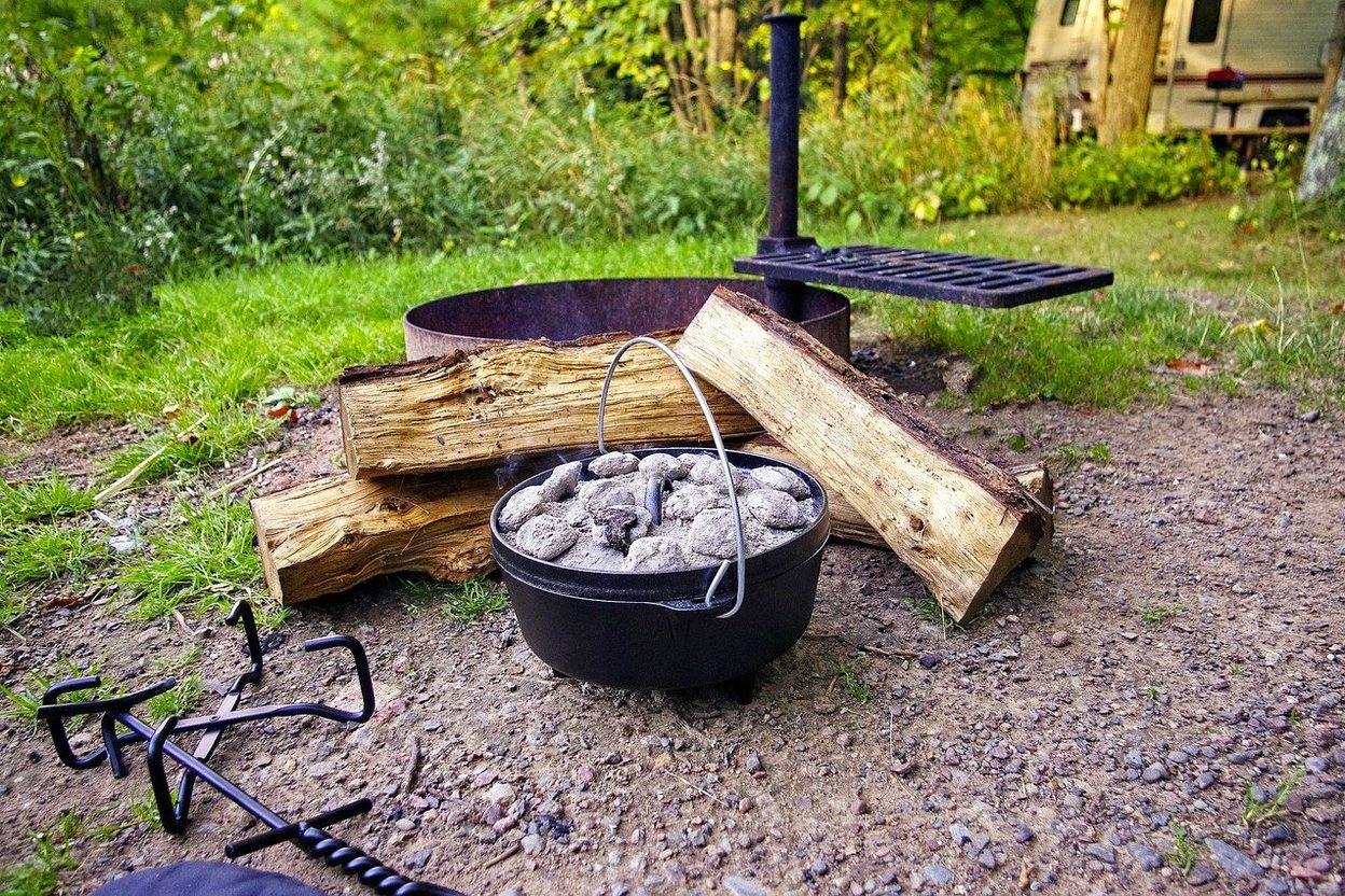 A flattened whole turkey on a cutting board beside a Dutch oven with glowing charcoal briquettes at a campsite picnic table.