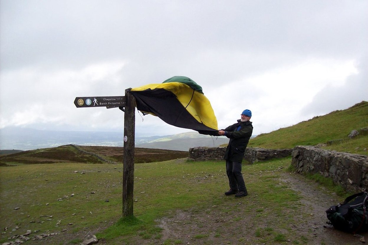 Hiker adjusting a yellow and black tent on a hillside trail sign.