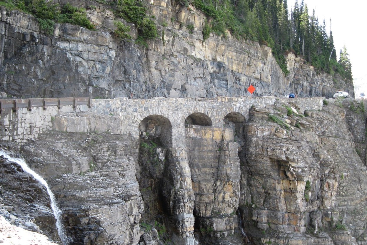 Switchbacks on Going-to-the-Sun Road cut into a mountainside in Glacier National Park, with a closure sign at the roadside.