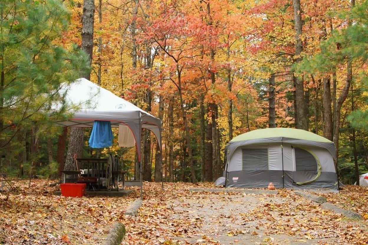 A tent set up with Halloween decorations at a crowded fall campground during the evening.
