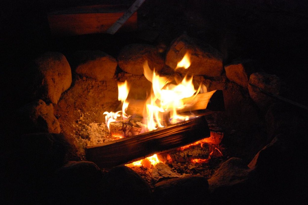 Campfire burning with logs and stones in a dark outdoor setting.