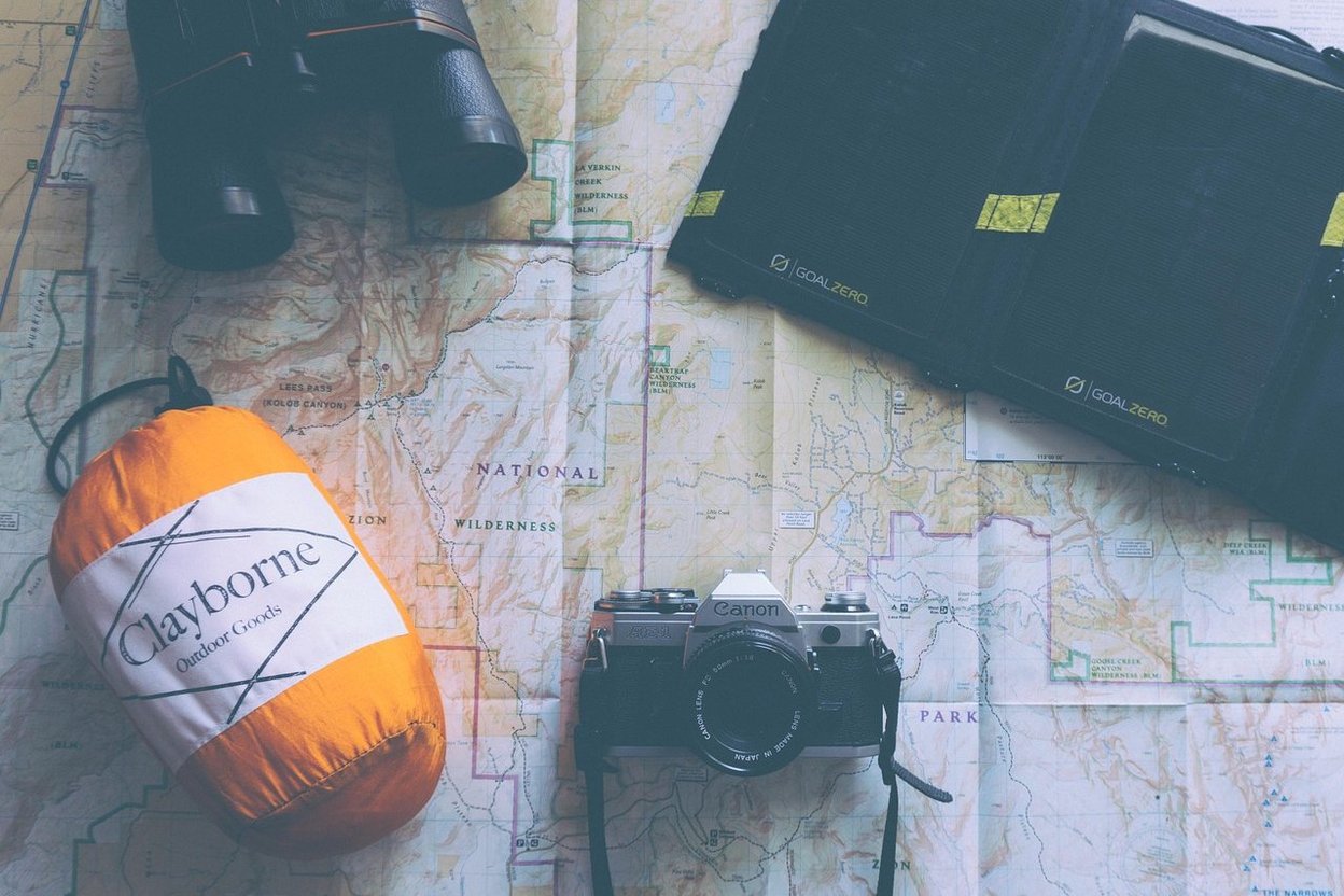 Outdoor gear including binoculars, camera, and sleeping bag on a topographic map.