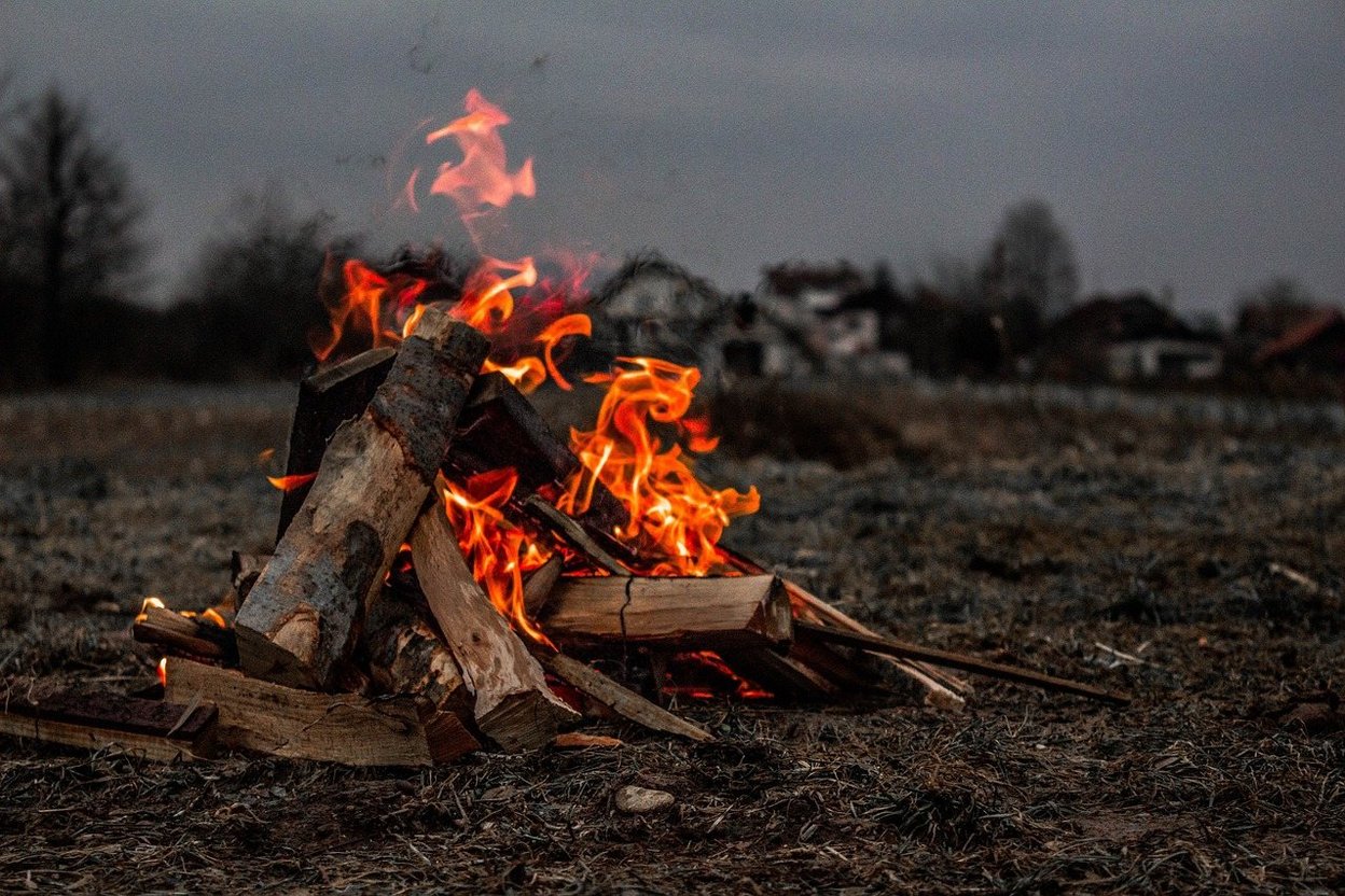 Campfire burning logs in a field at dusk.