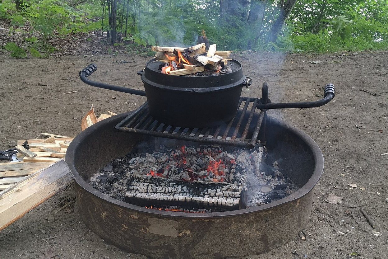 A Dutch oven cooking over coals on a campfire ring