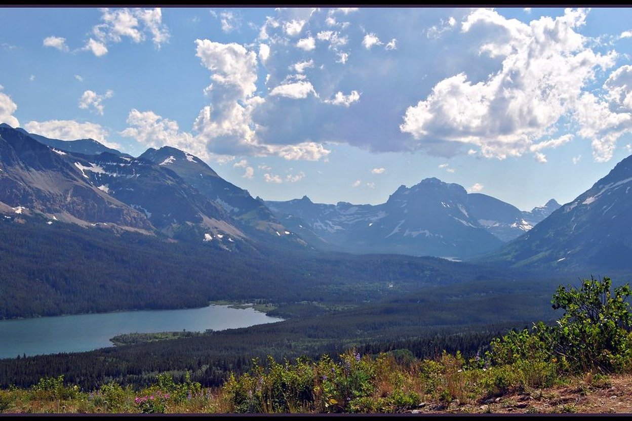 Two Medicine Lake in Glacier National Park with mountains rising behind the water and a closed-road sign at the valley entrance
