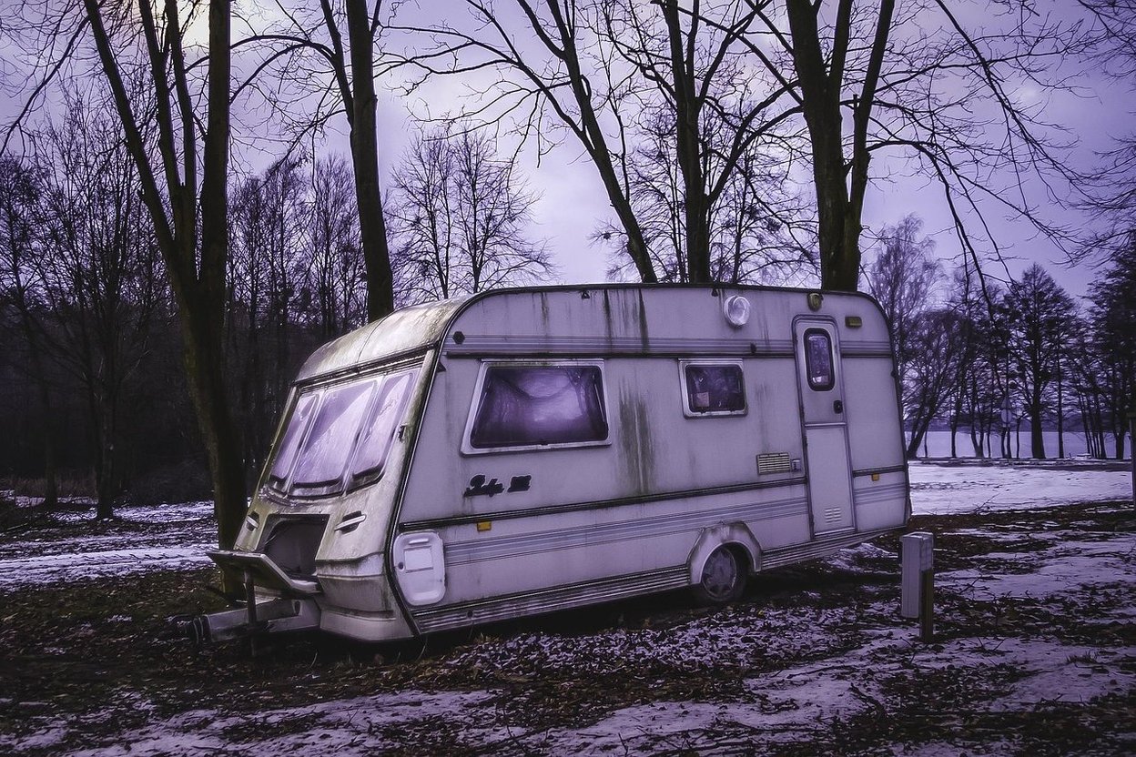 Abandoned camper trailer in snowy woods at dusk.