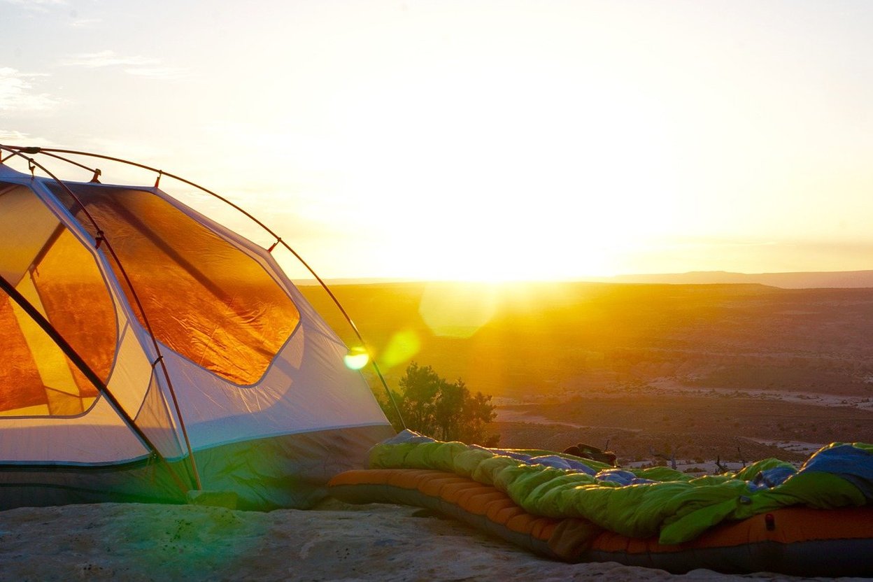 Tent and sleeping bag on a hill at sunrise.